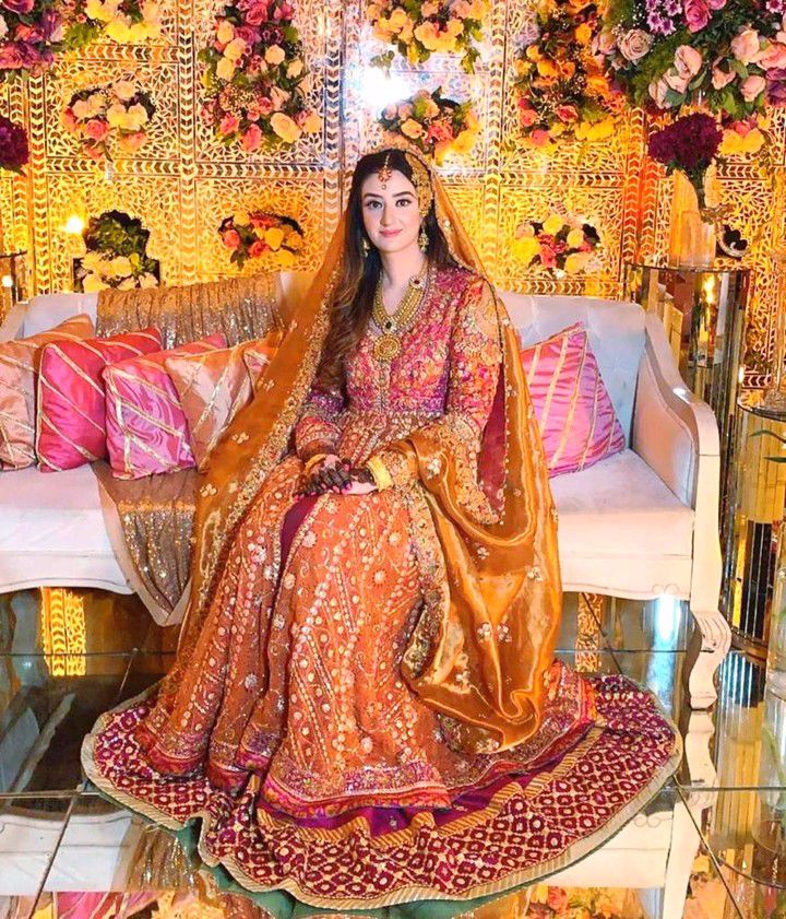 Minahil Buksh is resplendent in a signature #FarahTalibAziz kalidaar in burnt orange with a vibrant magenta lehnga, accentuated with gold embellishments and a stunning gold dupatta
